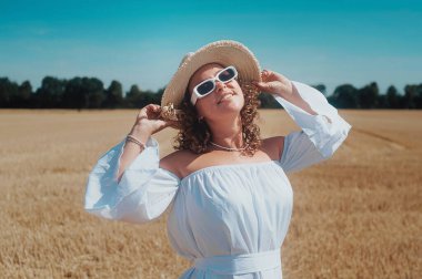 Beyaz elbiseli genç bir kadının portresi. Çayırda güneş gözlükleriyle poz veriyor.  