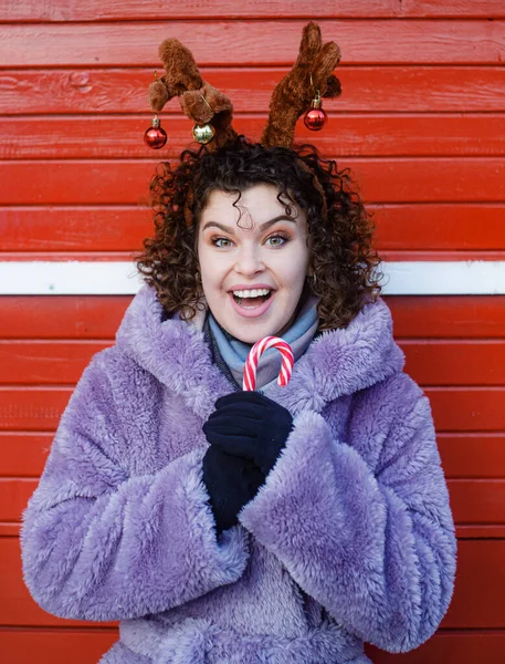 在圣诞节的背景下 微笑着拿着糖果的卷曲头发的女人 — 图库照片