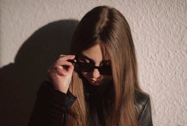 Deri ceketli, koyu arkaplanda gölgeli gözlüklü şık bir çocuğun portresi.