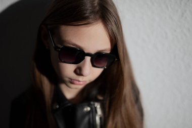 Deri ceketli, koyu arkaplanda gölgeli gözlüklü şık bir çocuğun portresi.