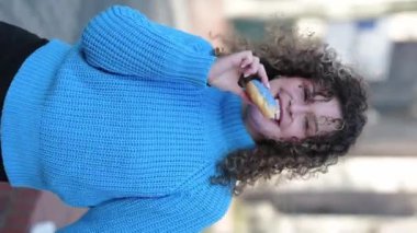 Kıvırcık saçlı, açık havada donut tutan komik bir genç kadın.