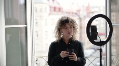 Kıvırcık saçlı kadın cep telefonuyla blogu için içerik oluşturuyor