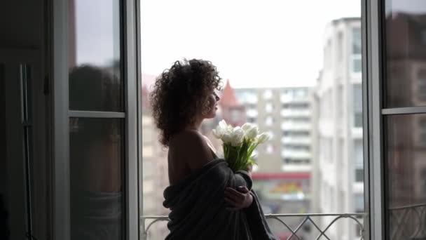 窓の近くに立っているカーリーヘアの女性 チューリップの花束 — ストック動画