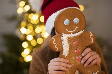 Noel Baba şapkalı çocuk Noel ağacı arka planında kış tatili için zencefilli ekmek yapıyor.