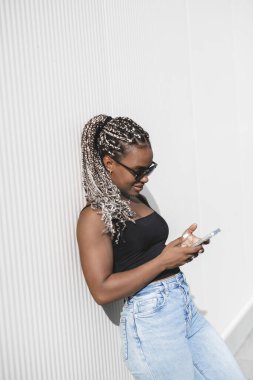 Beyaz bir arka planda telefonu olan uzun örgülü güzel Afro-Amerikan bir kadının portresi.