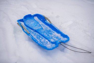 Taze karda dinlenen mavi bir kızağın yakın çekimi, kış aktivitelerinin eğlencesini ve heyecanını temsil ediyor.
