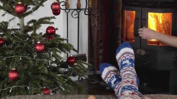 暖炉のそばのソファでリラックスしてください クリスマスツリーと暖炉 クリスマスソックスの女の子の足 — ストック動画