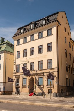 İsveç, Stockholm - 17 Temmuz 2022: Skeppsbron rıhtımındaki Hotel Gamla stan sarı klasik binasının kapatılması. Önünde ismi yazılı kahverengi bayraklar, kırmızı halı ve mavi gökyüzünün altında yayalar.