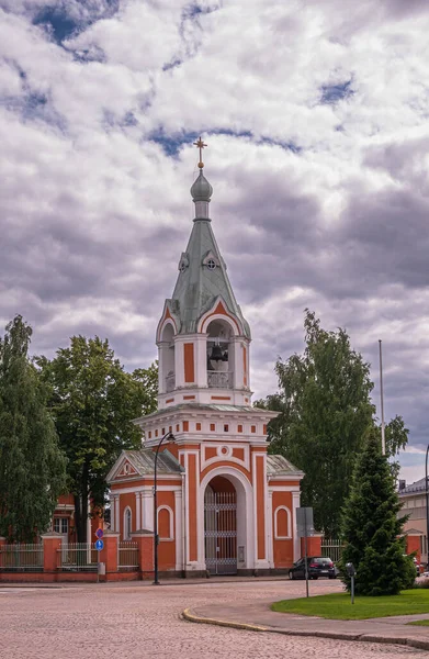 フィンランド ハミナ 2022年7月18日 赤と白のピーターとポール教会の鐘楼と緑の葉を持つ濃い灰色の雲の下の入り口 通りに車 — ストック写真