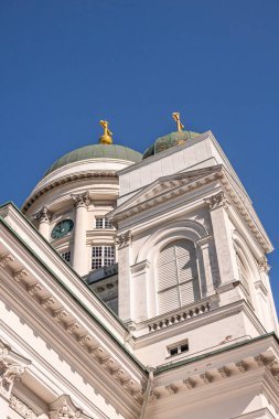 Helsinki, Finlandiya - 19 Temmuz 2022: Mavi gökyüzüne karşı beyaz taş katedralin SE köşesi. Altın tepeli küçük ve büyük yeşil kubbeye doğru bakıyor. Görünür saat