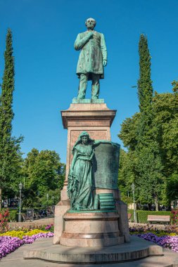 Helsinki, Finlandiya - 19 Temmuz 2022: Johan Ludvig Runeberg 'in yeşil Esplanadi parkında mavi gökyüzüne karşı sergilenen bronz heykeli. Finlandiya 'nın bakiresi yaya olarak heykel yapıyor. Renkli çiçekler