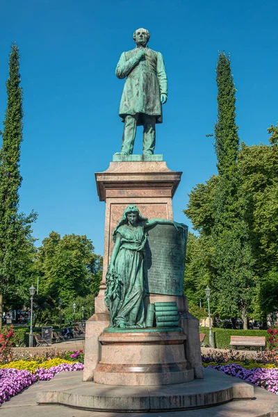 フィンランド ヘルシンキ2022年7月19日 ヨハン ルドヴィグ ルネベルクの正面青い空に対する緑のエスプラナディ公園に設置された台座の上にブロンズ像 徒歩でフィンランドの像の乙女 色とりどりの花 — ストック写真