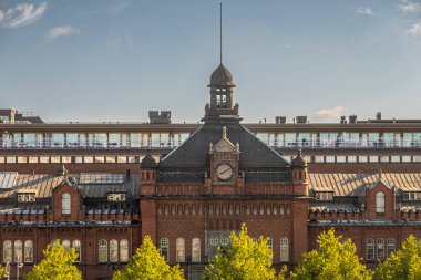 Helsinki, Finlandiya - 19 Temmuz 2022: Kırmızı tuğlalı tarihi gişe, gümrük deposu saat kulesinin açık mavi gökyüzü altındaki tesislere giriş ve çıkışını gösteriyor. Biraz yeşil yaprak..