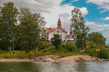 Helsinki, Finlandiya - 19 Temmuz 2022: Helsinki limanının girişinde mavi bulutların altında kendi yeşil adasında Kırmızı Çatılı Restoran Saaristo.