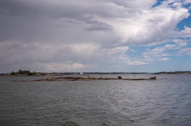 Helsinki, Finlandiya - 19 Temmuz 2022: Çıplak ve düz Rocky Pikkuluoto Adası 'nın önündeki gri deniz suyunda, yağmurlu bulutların altında. Arkadaki tekne trafiği.