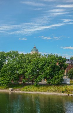 Helsinki, Finlandiya - 19 Temmuz 2022: Suomenlinna Kalesi. Yeşil kubbeli kilise kulesi mavi bulutların altında yeşil ağaç yapraklarının üzerinde. Kısmen gizlenmiş kırmızı tuğla bina