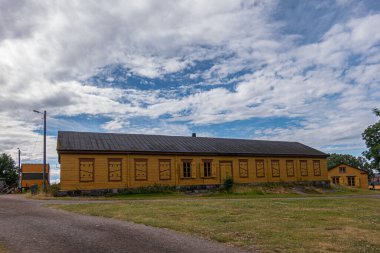 Helsinki, Finlandiya - 19 Temmuz 2022: Suomenlinna Kalesi. Çoğu penceresi mavi bulutların altında olan uzun sarı bir bina. Önde yeşil çimenler ve çakıllar var.