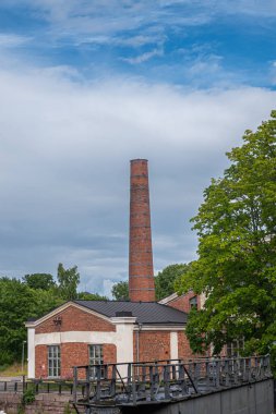 Helsinki, Finlandiya - 19 Temmuz 2022: Suomenlinna Kalesi. Uzun kırmızı tuğlalı bacalı Lavyhalli binası mavi bulutların üzerinde. Yeşil yeşillik ve su kilidi kapısı Viaporin tersanesinin önünde.