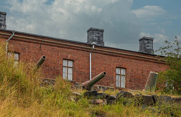 芬兰赫尔辛基 2022年7月19日 Suomenlinna Fortress 阿尔芒海岸 大炮指向蓝色云彩下历史性的红砖建筑前面的大海 悬崖上的绿色杂草 — 图库照片
