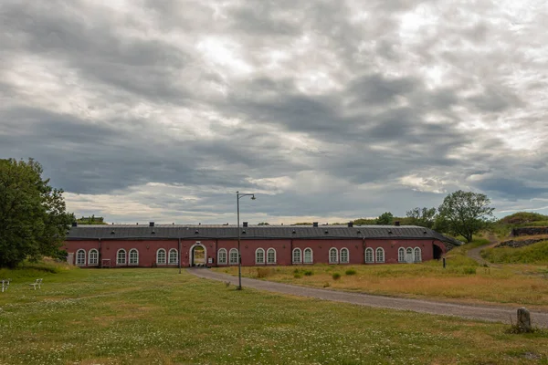 フィンランドのヘルシンキ 2022年7月19日 スオメリンナ要塞 兵士のための長い赤の歴史的な石の住居の建物 今日ノルディック文化センター Hiap 灰色の雲の下で 黄色の牧草地に設定 — ストック写真