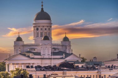 Helsinki, Finlandiya - 19 Temmuz 2022: Sarı-gri bulutların altında şehir manzarası olan beyaz taş katedralin üzerinde altın gün batımına yakın çekim