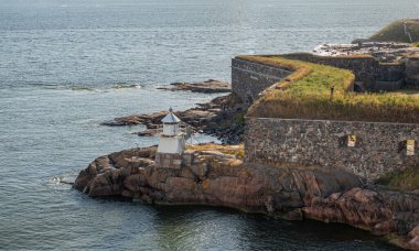 Helsinki, Finlandiya - 20 Temmuz 2022: Suomenlinna Kalesi. Royal Gate Adası 'nın SE köşesindeki kayalık sahil şeridinde surların altında beyaz ışık feneri. Açık mavi deniz suyu