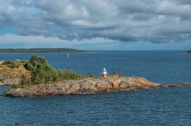 Helsinki, Finlandiya - 20 Temmuz 2022: Suomenlinna Kalesi. Geniş manzara. Reimarisaar adasındaki kısa ışık feneri mavi denizin altında, kalın mavi bulutların altında. Biraz yeşil bitki