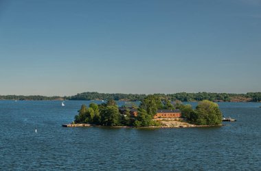 Helsinki, Finlandiya - 20 Temmuz 2022: Ravintola restoranı açık mavi gökyüzünün altındaki koyu mavi denizde kendi küçük yeşil adası Lonna 'da. Ufukta ana orman kuşağı görünüyor.