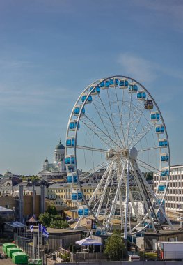 Helsinki, Finlandiya - 20 Temmuz 2022: Tarihi liman. Skywheel dönme dolap, mavi gökyüzünün altında yeşil kubbeleri olan beyaz katedralle yakınlaşıyor. Dağınık otoparklar ve öndeki binalar
