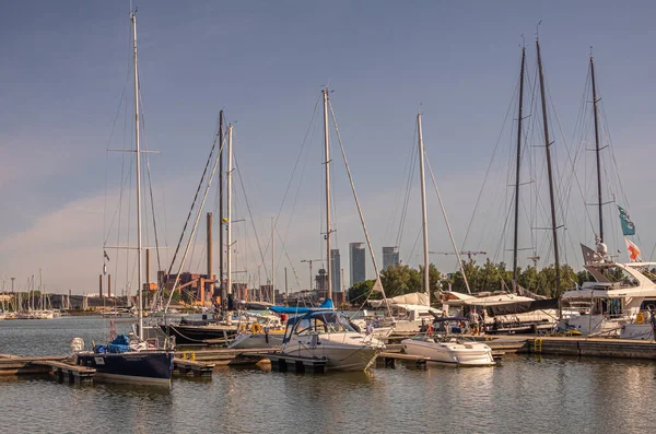 Helsinki, Finlandiya - 20 Temmuz 2022: Pohjoissatama Limanı. Bir sıra yelkencilik ve... Motorlu tekneler rıhtıma yanaştı. Hanasaari Enerji Santrali bacaları ve mavi gökyüzünün altında konut kuleleri