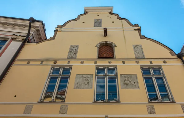 stock image Estonia, Tallinn - July 21, 2022: Pikk 26, street is Historic yellow facade of House of the Brotherhood of Black Heads with several gray cement mural sculptures between windows under blue sky