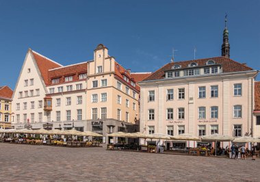 Estonya, Tallinn - 21 Temmuz 2022: Belediye binasının kuzey tarafındaki restoranlar ve barlar, mavi gökyüzü altında bej cepheli modern mimariler sunuyor. Patiolar ve insanlar