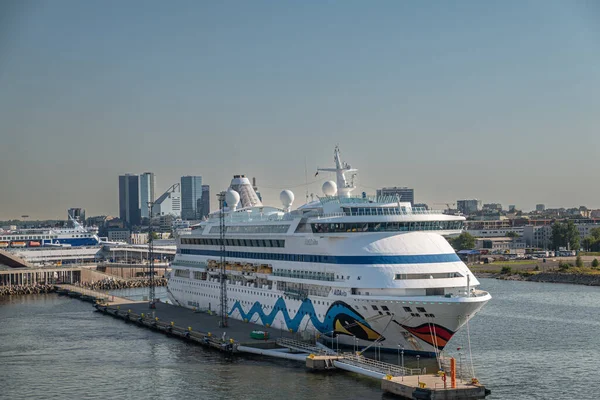 stock image Estonia, Tallinn - July 21, 2022: Closeup of white Aidavita cruise ship docked in port with high rise cityscape in back under light blue sky. Wider port industry around.