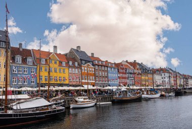 Kopenhag, Danimarka - 23 Temmuz 2022 Nyhavnn restoran sırasının renkli cephelerinin üzerinde yoğun bulut mavi bulutların altında suyun kuzey tarafında. Turist gezisi teknesi, yayalar ve bayraklar