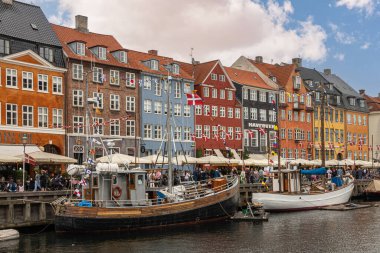 Kopenhag, Danimarka - 23 Temmuz 2022 Nyhavnn restoran sırasının renkli cephelerinde tekneler suyun kuzey tarafında mavi bulutların altında. Yelkenliler, yayalar ve bayraklar