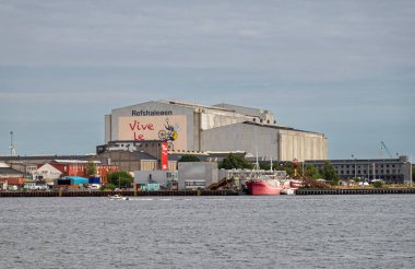 Kopenhag, Danimarka - 24 Temmuz 2022: Büyük ve uzun boylu eski fabrika, şimdi limanın doğu yakasında açık mavi gökyüzü altında spor ve macera alanı Refshaleoen. Fransa turu reklamı duvarda