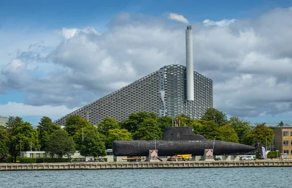 丹麦哥本哈根 2022年7月24日 在海军基地的海事博物馆里 在黑色海军潜艇的后面 有一个冒着烟的烟囱的高山滑雪场 蓝云和绿叶带 — 图库照片