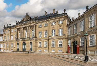 Kopenhag, Danimarka - 24 Temmuz 2022: Kahverengi taş Frederik Sarayı ve mavi bulutlar altında Amalienborg 'da ek kanat. Pediment heykelleri, sütunları ve klasik mimarisi olan kahverengi taşlar.