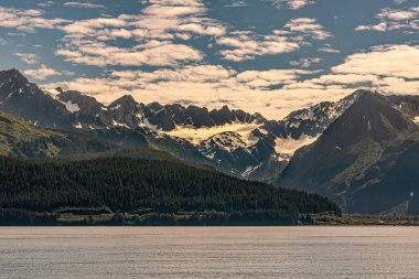 Seward, Alaska, ABD - 22 Temmuz 2011: Diriliş Körfezi kıyı şeridinden yeşil orman kanatları, yüksek dağ sıraları ile kaplı çatlaklar ve mavi bulutların altında keskin tepeler