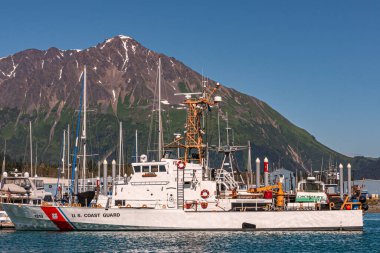 Seward, Alaska, ABD - 22 Temmuz 2011: Kapanış, Beyaz Sahil Güvenlik gemisi mavi gökyüzü altında rıhtıma demir attı. Yeşil ormanlık kanatlı gri dağ ve arkasında kar parçaları var.