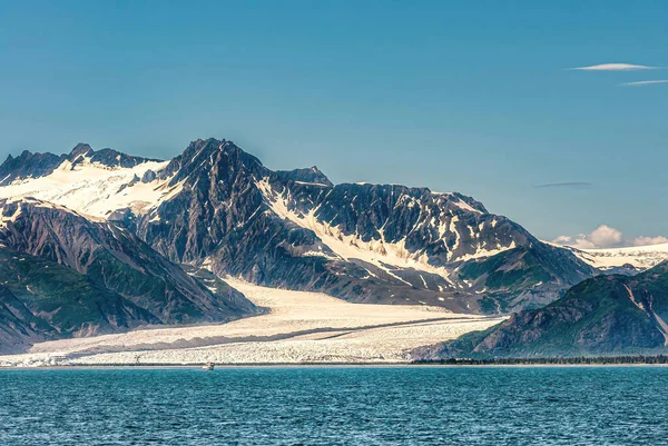 2011年7月22日 氷河が青い空の下で湾の水に到達します 暗い岩の山の範囲にたくさんの雪のパッチ 青い水を前に — ストック写真