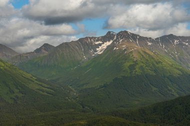 Girdwood Alaska, ABD - 23 Temmuz 2011: Chugach Park. Kasabanın yukarısındaki yoğun mavi bulutların altında kar yamaçları ve yeşil orman kanatları olan geniş bir dağ sırası.