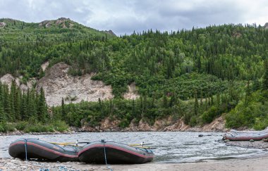 Denali Park, Alaska, ABD - 24 Temmuz 2011: Nenana Nehri üzerinde rafting. Nenana Nehri kıyısındaki Alaska Raft botlarının arkasında yeşil ormanlık dağ kanadı var. Gri su mavi bulut