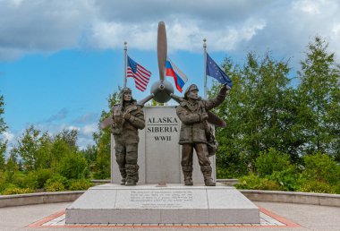 Fairbanks, Alaska, ABD - 27 Temmuz 2011: Alaska Sibirya 2. Dünya Savaşı Anıtı gri-mavi bulutlar altında ve arkada yeşil yapraklar. Pervanenin arkasındaki ulusal bayraklar