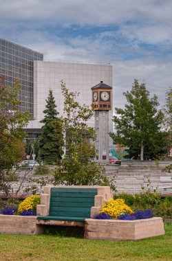 Fairbanks, Alaska, ABD - 27 Temmuz 2011: Mavimsi bulutlar altında Golden Heart Plaza 'daki Rotary Club Clock Tower. Etrafta yeşil yapraklar ve çiçekler var. Arkadaki Uzun Rabinowitz Adliyesi