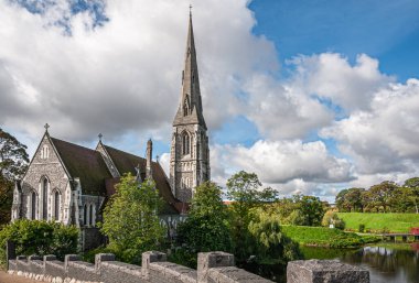 Kopenhag, Danimarka - 13 Eylül 2010: Kastellet 'in yeşil surları ile gri taş St. Albans Kirke, kilise, mavi bulutların altında ince çan kulesi