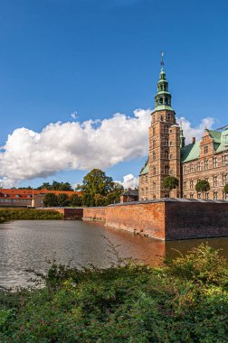 Kopenhag, Danimarka - 13 Eylül 2010: Kırmızı tuğlalı Rosenborg Slot hendeği üzerindeki SW bakış açısı baskın kule ve mavi bulutlar altında surlar. Önde yeşil yapraklar var.
