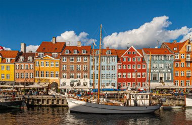 Kopenhag, Danimarka - 13 Eylül 2010: İkonik Nyhavn restoran cepheleri mavi bulutlar altında iskele boyunca parlak renklerde. Sudaki tekneler. İnsanlar yürüyor ve oturuyor.