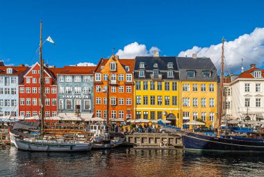 Kopenhag, Danimarka - 13 Eylül 2010: Nyhavnsbroen 'da açık renkli Nyhavn restoran cepheleri mavi bulutlar altında. Sudaki tekneler. İnsanlar yürüyor ve oturuyor.