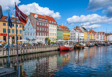 Kopenhag, Danimarka - 13 Eylül 2010: İkonik Nyhavn restoran cepheleri mavi bulutlar altında parlak renklerde. Bayraklar, yürüyen ve oturan insanlar. Kanal suyunda tekneler